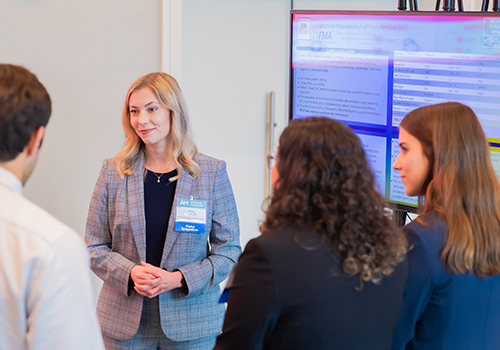 A female judge smiles as a group of students present their poster for the FMA poster symposium