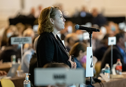 A female physician stands a a microphone to provide testimony