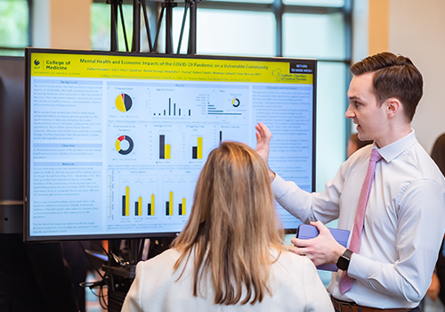 Judge listening to a student present his poster for the FMA poster symposium