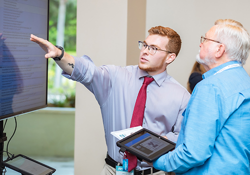 Poster Symposium image of a male student presenting his poster to a judge